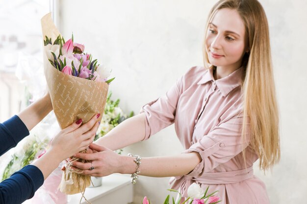 Photo delivery of a floral workshop. the customer receives his order-a bouquet of pink tulip. hand florist pass flowers to the buyer