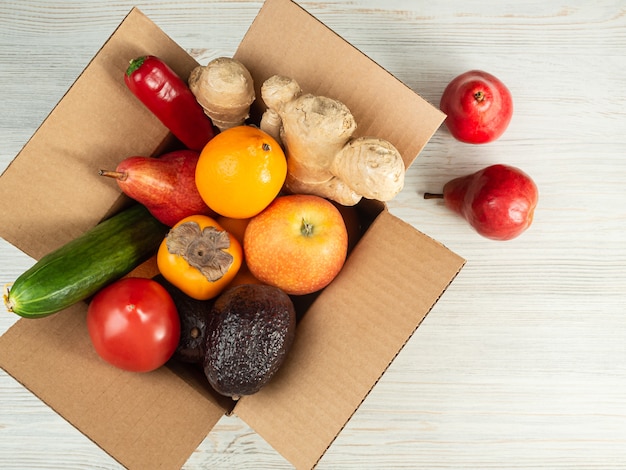 Delivery of fruits and vegetables in a corton box, the box is open, on a wooden table, top view.