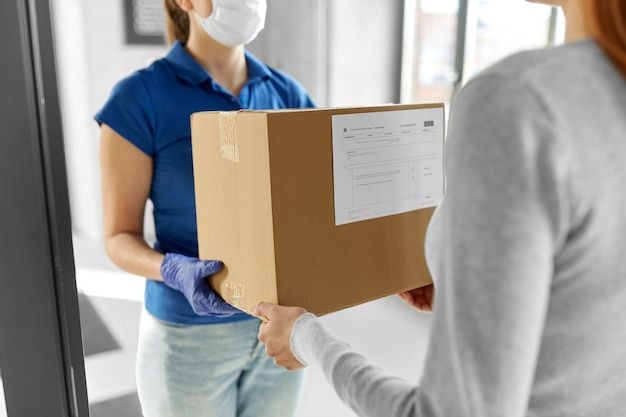 フェイスマスクを着た配達女の子が女性に荷物を送る