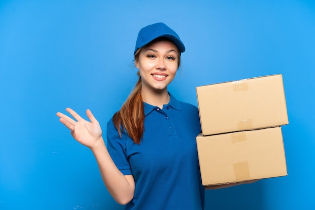 Delivery girl over isolated blue wall extending hands to the side for inviting to come