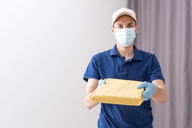 Delivery guy with protective mask and gloves holding box with groceries.