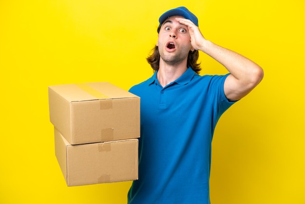 Delivery handsome man isolated on yellow background doing surprise gesture while looking to the side