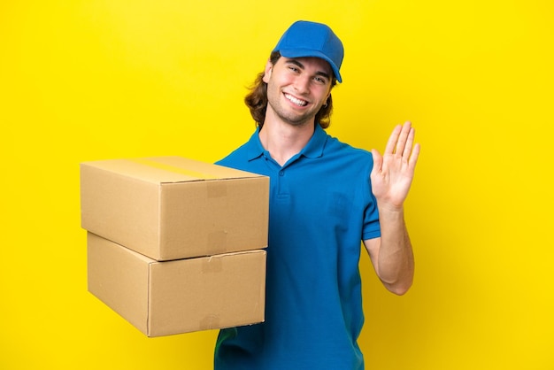 Delivery handsome man isolated on yellow background saluting with hand with happy expression