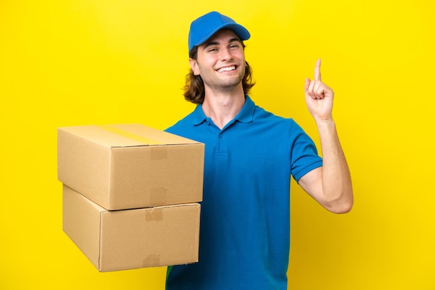 Delivery handsome man isolated on yellow background showing and lifting a finger in sign of the best