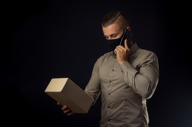 Delivery to home. Man with phone and package over black wall