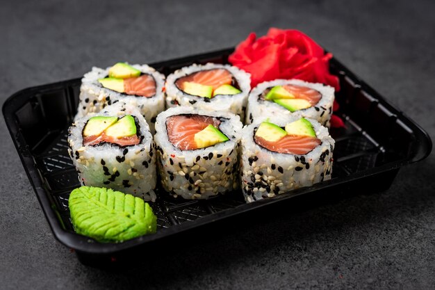 Delivery of Japanese traditional food. Salmon and avocado rolls with black and white sesame seeds in a plastic container