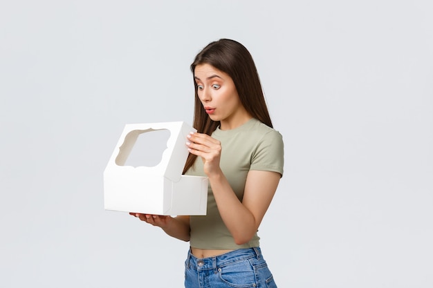 Consegna, stile di vita e concetto di cibo. sorridente ragazza felice aprire la scatola bianca con dolci deliziosi dessert, torta o muffin ordinato nella migliore pasticceria, in piedi sfondo bianco.