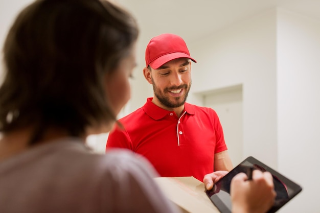 Foto concetto di consegna, posta, persone e spedizione - uomo felice che consegna la cassetta dei pacchi e firma del cliente sul computer tablet pc a casa