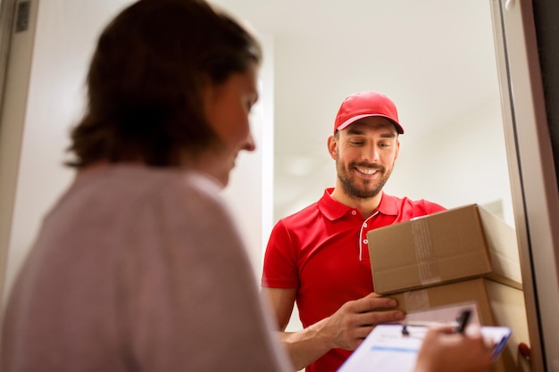 配送、郵便、人、配送のコンセプト – 自宅の顧客署名フォームに小包箱を届けるクリップボードを持つ幸せな男