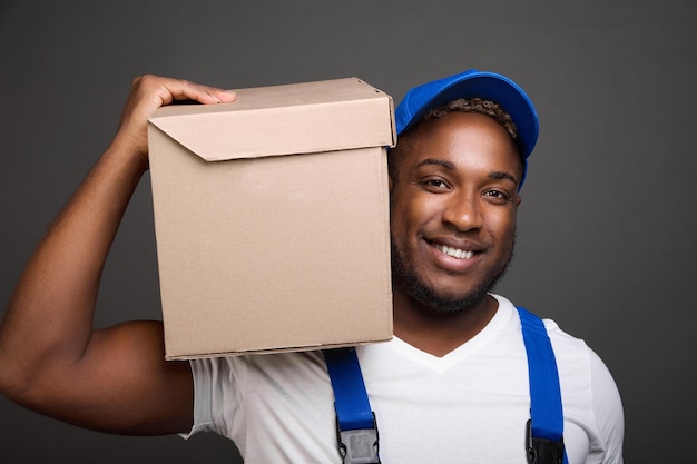 Delivery man in baseball cap holding and carrying cardboard box on his shoulder