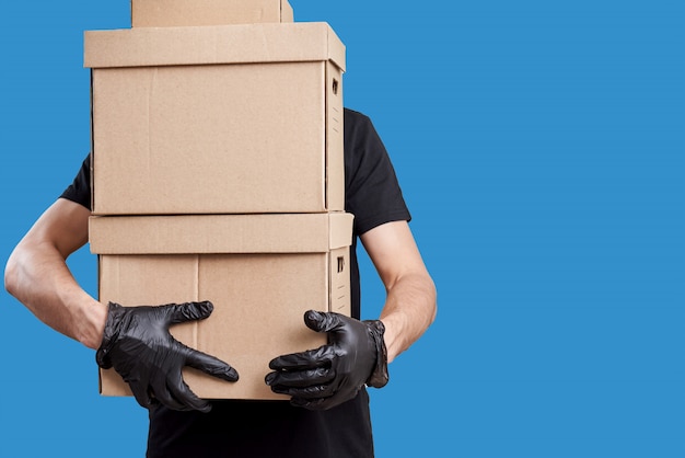 Delivery man in black uniform with medical gloves and protective mask hold cardboard box