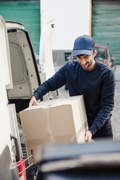 Uomo di consegna che trasporta la scatola di cartone dal veicolo