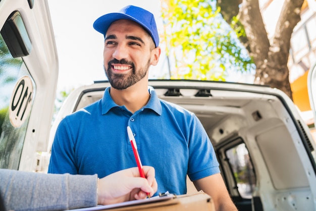 Delivery man carrying package while customer sign in clipboard