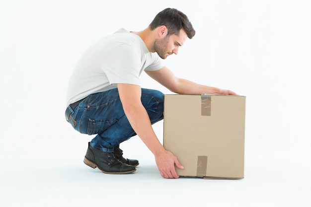 Delivery man crouching while picking cardboard box