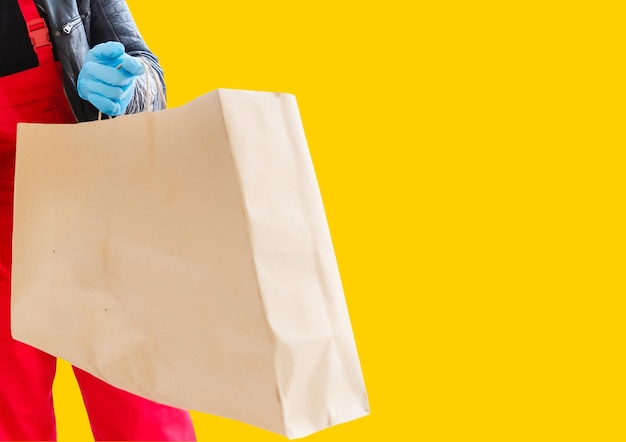 Delivery man employee in mask glove hold craft paper packet with food isolated on yellow background studio Service quarantine pandemic coronavirus virus 2019-ncov concept.