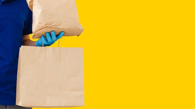 Delivery man employee in mask glove hold craft paper packet with food isolated on yellow background studio Service quarantine pandemic coronavirus virus 2019-ncov concept.