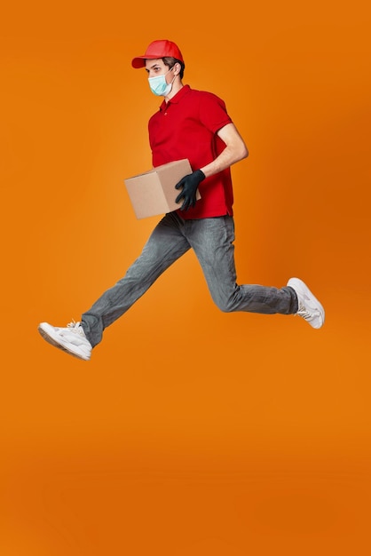 Delivery man in face mask holding cardboard box and jumping