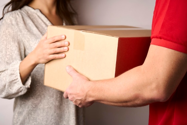 Delivery man giving cardboard box to female hand