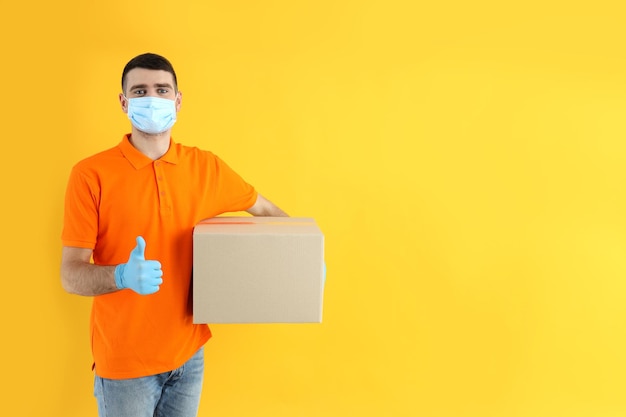 Delivery man in gloves and mask holds box on yellow background