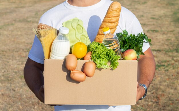 Uomo di consegna che tiene la scatola con generi alimentari freschi all'aperto