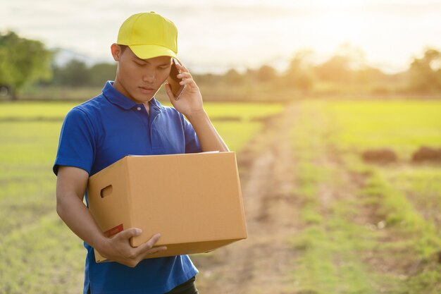 Delivery man holding brown parcel or cardboard boxes delivery to customer at countryside 