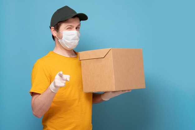 Delivery man holding cardboard box in medical rubber gloves and mask pointing on you Online shopping and