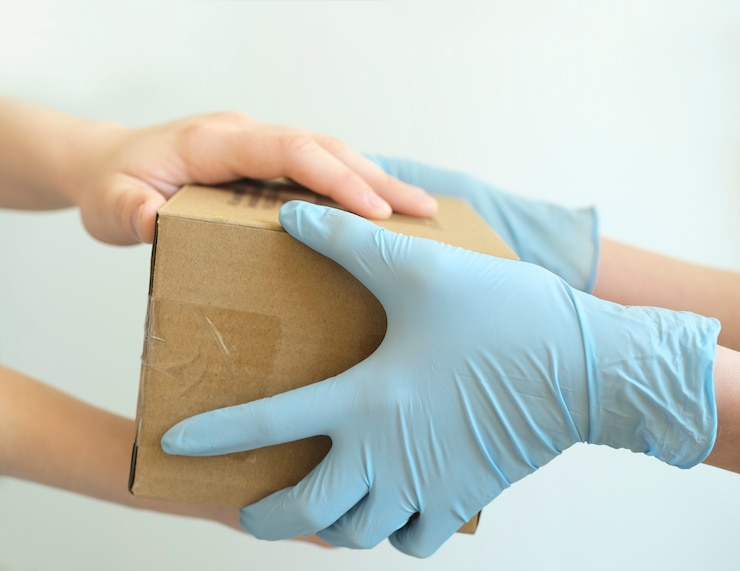 Delivery man holding cardboard boxes in medical rubber gloves.