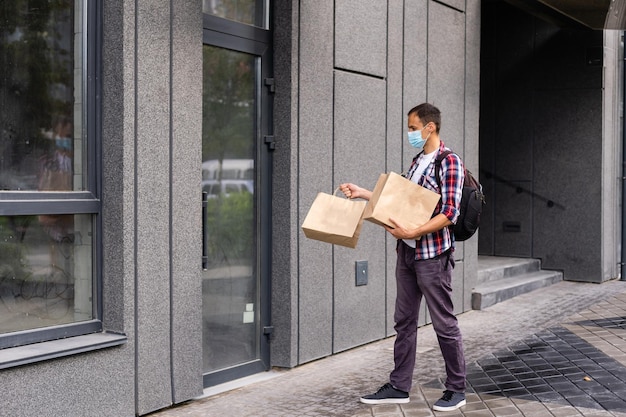 Delivery man holding paper bag with food, food delivery man in protective mask