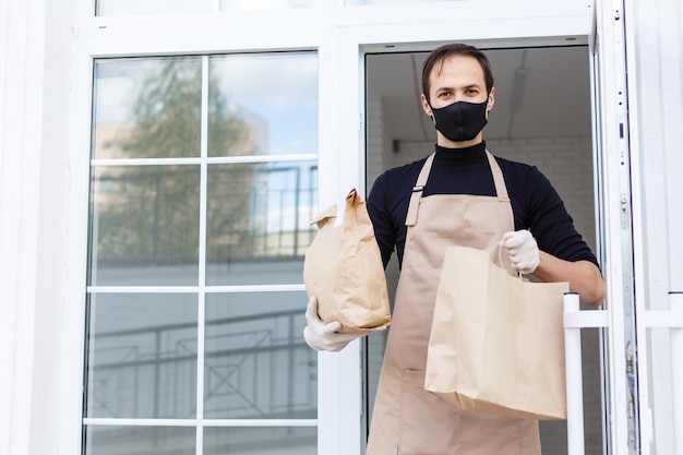 Delivery man holding paper bag with food, food delivery man in protective mask