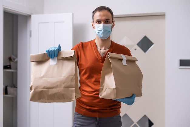 Delivery man holding paper bag with food on white background, food delivery man in protective mask.