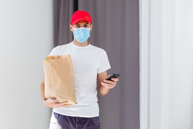 Delivery man holding paper bag with food on white background, food delivery man in protective mask