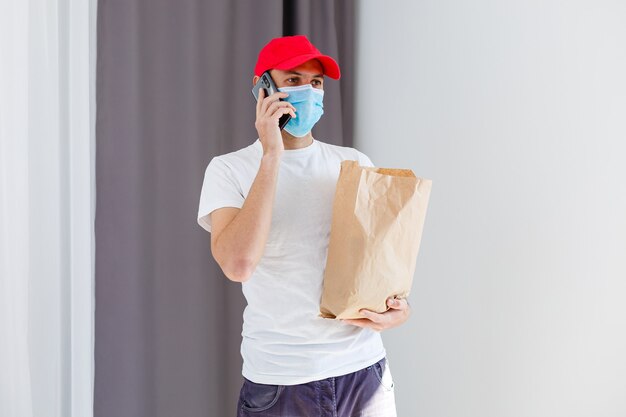 Photo delivery man holding paper bag with food on white background, food delivery man in protective mask