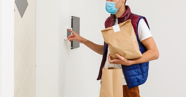 Delivery man holding paper bag with food on white background, food delivery man in protective mask