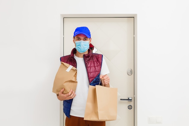 Delivery man holding paper bag with food on white background, food delivery man in protective mask