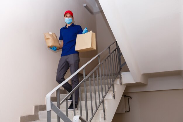 Delivery man holding paper bag with food on white entrance of house background , food delivery man in protective mask