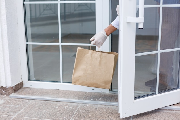 Delivery man holding paper bag with food on white entrance of house background , food delivery man in protective mask