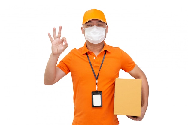 Delivery man holding parcel box and wearing protective mask for prevent virus Covid-19 and showing ok isolated on white wall, Online shopping shipment and fast express delivery service concept