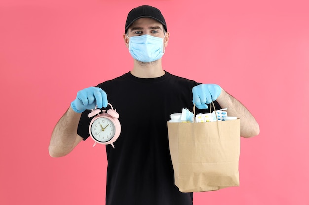 Delivery man holds bag with medicines and alarm clock on pink background