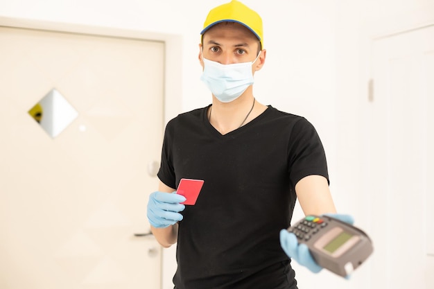 Delivery man holds bank payment terminal to process acquire credit card payments. employee in cap t-shirt working courier. service concept