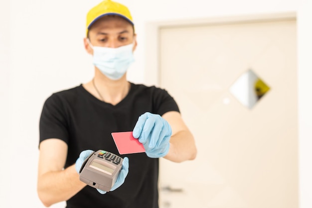 Delivery man holds bank payment terminal to process acquire credit card payments. Employee in cap t-shirt working courier. Service concept.