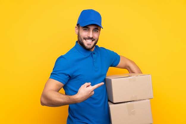 Delivery man over isolated yellow and pointing it