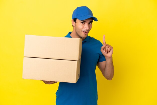 Delivery man over isolated yellow wall intending to realizes the solution while lifting a finger up