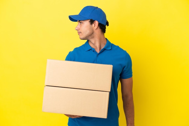 Delivery man over isolated yellow wall looking to the side