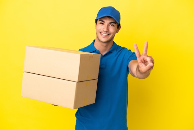 Delivery man over isolated yellow wall smiling and showing victory sign