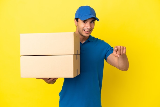 Delivery man over isolated yellow wall surprised and pointing front