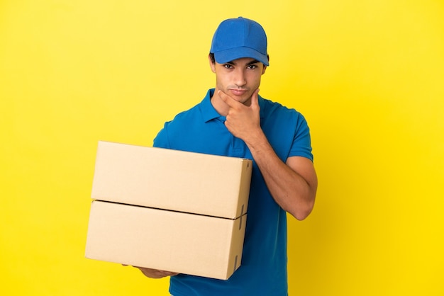 Delivery man over isolated yellow wall thinking