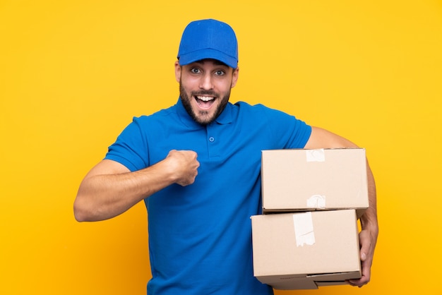 Delivery man over isolated yellow with surprise facial expression