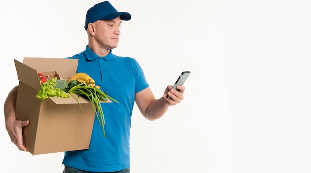 Delivery man looking at smartphone while carrying grocery box