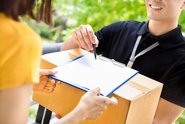 Delivery man pointing on the document showing where to sign, while delivering parcel box to a woman