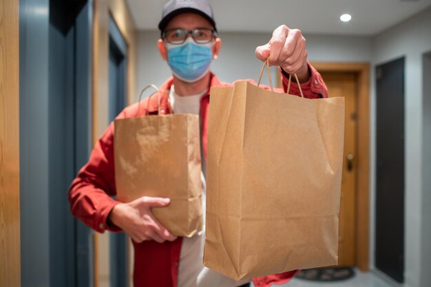 Photo delivery man in protective mask holding paper bag with food in the entrance the courier gives the box with fresh vegetables and fruits to the customer